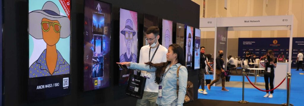 Two attendees examining a display of NFT artwork at The Blockchain Economy London Summit